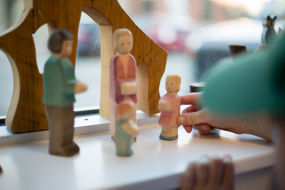 A child's hand arranging painted wooden toy figures on a windowsill