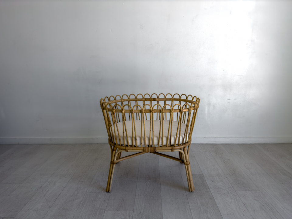 An empty wicker bassinet with a thin mattress in a bright room