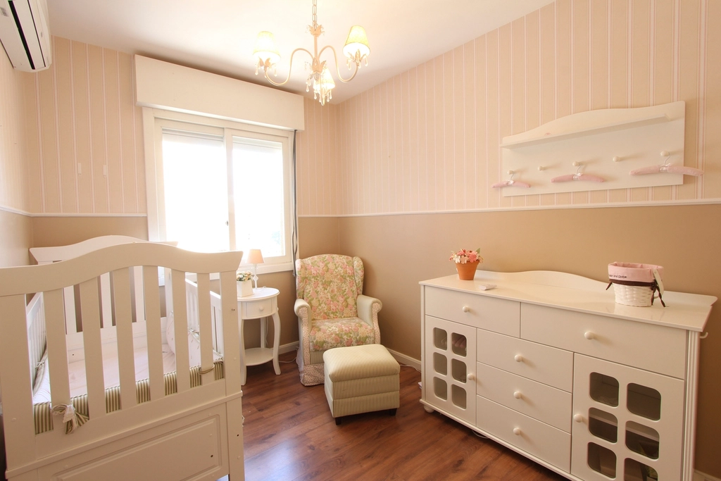 A nursery with a white crib, an armchair and a white chest of drawers